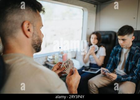 Padre che gioca a carte con figlio e figlia seduti in treno Foto Stock