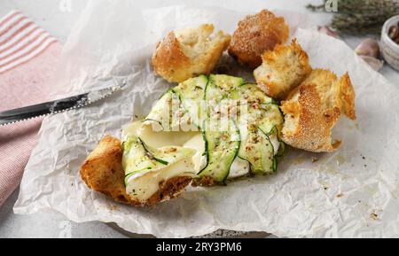Formaggio Brie camembert al forno con zucchine con noci, erbe e olio d'oliva. Servito con vino e pane Foto Stock