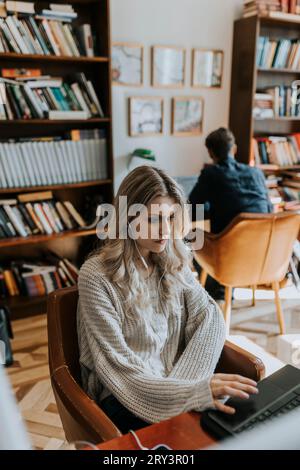 Giovane donna bionda che usa un notebook mentre è seduta in biblioteca Foto Stock
