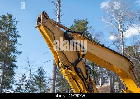 Tubi e tubi flessibili idraulici e a gomito del braccio dell'escavatore su una macchina per attrezzature pesanti da lavoro, in un nuovo cantiere edile, con cielo e albero blu Foto Stock