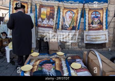 Un ebreo ultra ortodosso usa il distributore automatico di biglietti (ATVM) mentre si trova in mezzo a souvenir con immagini di leader spirituali ebrei in vendita nel mercato Mahane Yehuda a Gerusalemme Ovest in Israele Foto Stock