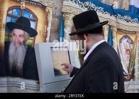 Un ebreo ultra ortodosso usa il distributore automatico di biglietti (ATVM) mentre si trova in mezzo a souvenir con immagini di leader spirituali ebrei in vendita nel mercato Mahane Yehuda a Gerusalemme Ovest in Israele Foto Stock