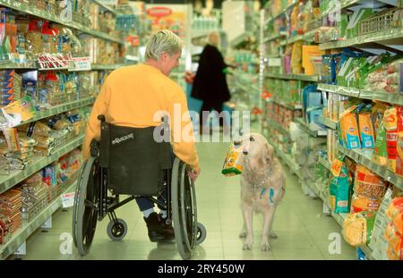 Paziente in sedia a rotelle e cane di servizio che fa la spesa nel supermercato, paziente in sedia a rotelle e cane di servizio che fa la spesa nel supermercato, mammiferi Foto Stock