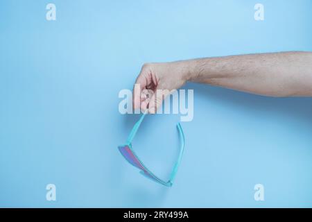 La mano di un uomo che regge occhiali da sole blu Foto Stock