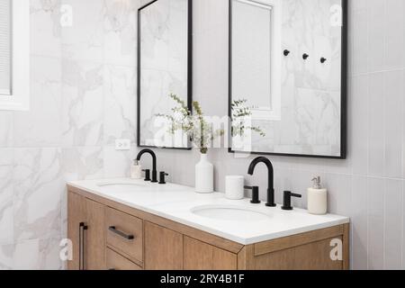 Un bagno con marmo e piastrelle verticali sovrapposte della metropolitana, un mobile vanity bianco in quercia, specchi e rubinetti quadrati con cornice nera e ripiano in marmo. Foto Stock