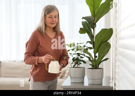 Donna anziana che annaffiava bellissime piante in vaso a casa Foto Stock