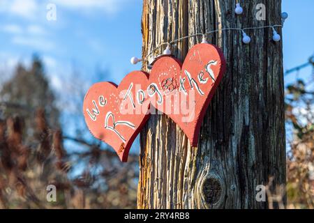 Due cuori rossi dipinti con le parole "We R Together" esposte su un palo di legno a Vancouver, Canada Foto Stock