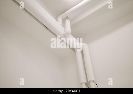 Messa a fuoco selettiva, dettaglio ravvicinato e vista interna del sistema di tubazioni verniciate di bianco allestito su angolo, soffitto e parete. Foto Stock