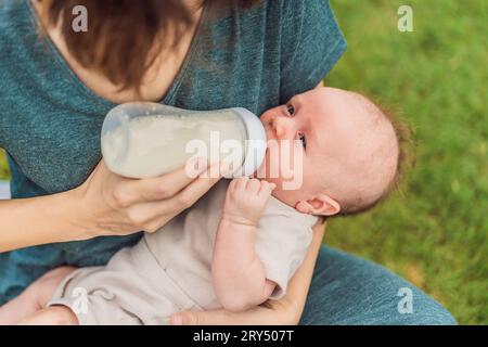 La madre tiene in mano e allatta il bambino dal biberon nel parco. Ritratto di un neonato carino che viene nutrito dalla madre con il biberon. Una donna amorevole che dà Foto Stock