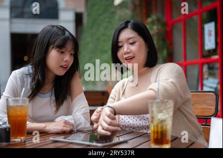 Due giovani amiche asiatiche felici si divertono a parlare mentre si rilassano a un tavolo all'aperto in una caffetteria in città. Stile di vita e patatine fritte Foto Stock