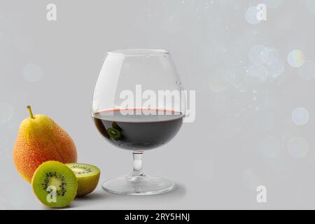 Un'immagine accattivante che mostra un bicchiere di vino fresco pieno di ricco vino rosso, accompagnato da fette di kiwi e pere. Rimane isolato contro una S. Foto Stock