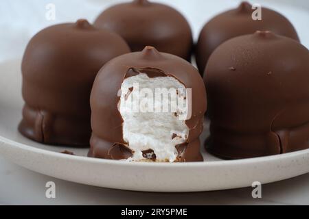 Marshmallow ricoperto di cioccolato. Krembo sul tavolo con un biscotto. Classico spuntino d'infanzia israeliano Krembo. Foto Stock