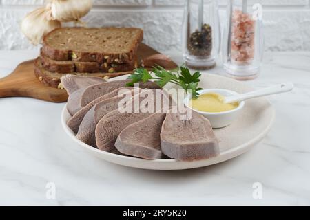 Fette di lingua di manzo bollita a fette su piatto bianco con senape Foto Stock