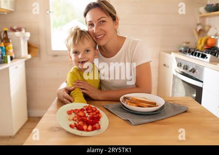 stile di vita, giovani madri e figli seduti al tavolo in cucina con piatti di cibo Foto Stock