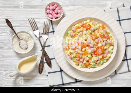Insalata Ambrosia con ananas, arance mandarine, yogurt, mini marshmallow, cocco e panna montata in ciotola bianca su tavolo di legno bianco con ingresso Foto Stock