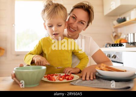 Allegra madre caucasica e figlioletto sono seduti in cucina e preparano la colazione Foto Stock