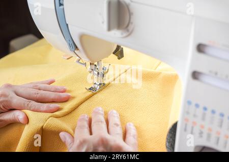 Cucitura a mano di tessuti gialli su una moderna macchina da cucire sul luogo di lavoro in atelier. Le mani delle donne cuciscono pezzi di tessuto sul primo piano della macchina da cucire. H Foto Stock