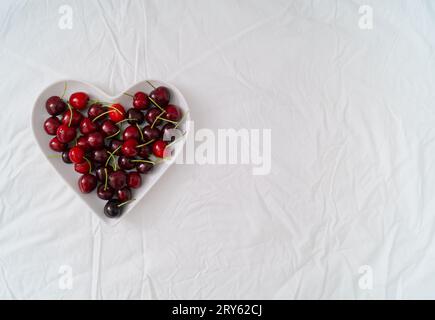 Design creativo a forma di cuore fatto di ciliegie rosse. Frutta estiva minimalista. Idea d'amore piatta. Estetica Cherry. Copia spazio. Foto Stock