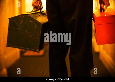 Vista posteriore ritagliata di un uomo che trasporta due cassette degli attrezzi in un corridoio. Foto Stock