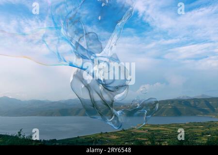 Gigantesca bolla di sapone colorata che si snoda di fronte al lago e alle montagne Foto Stock