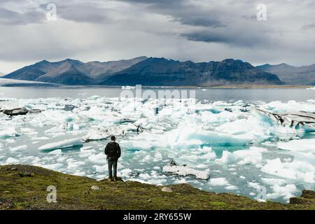 L'uomo si affaccia sulla laguna glaciale con montagne e iceberg Foto Stock