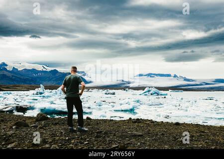 L'uomo cammina lungo le rocce sul lato della laguna glaciale e del ghiacciaio Foto Stock