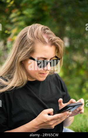 Giovane donna guarda con attenzione uno smartphone nel parco Foto Stock