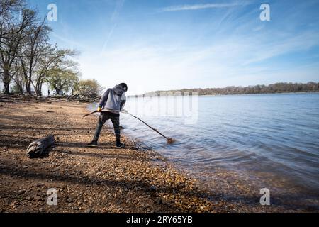 Ragazzo che gioca con il bastone sulla costa del lago in inverno. Foto Stock