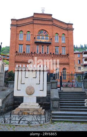 Vista esterna con grande menorah bianca in pietra e marmo. Presso la grande sinagoga ebraica di mattoni rossi a Tbilisi, Georgia, Europa. Foto Stock