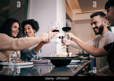 Tre donne vestite casualmente, tra cui una afro-americana, e un uomo, alzano i bicchieri da vino per un brindisi in un ristorante fusion. Angolo basso sh Foto Stock