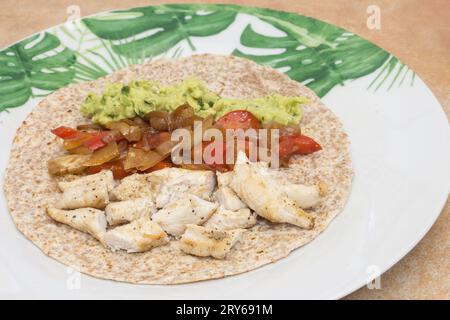 Una tortilla Fajita di pollo di grano intero aperta servita su un piatto adornato con foglie verdi, il tutto in un ambiente rustico da cucina con succulento stagionato Foto Stock