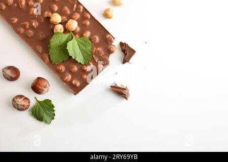 Dettaglio della barretta di cioccolato al latte con nocciole su tavola bianca con noci e foglie intorno. Vista dall'alto. Foto Stock