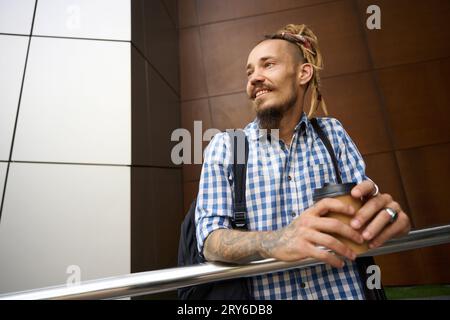 Happy Man si erge con un bicchiere di caffè all'esterno di un edificio moderno Foto Stock