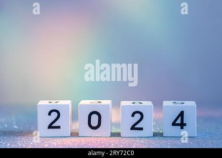 Capodanno 2024 in arrivo. Blocchi in legno bianco con numero 2024 su texture glitter in luce neon Foto Stock