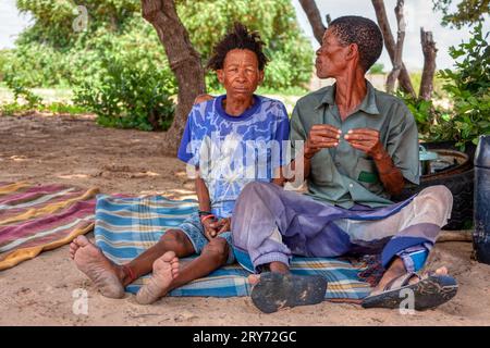 Un vecchio bushman san del Kalahari centrale, villaggio di New Xade in Botswana, di fronte al suo cortile seduto con la moglie Foto Stock