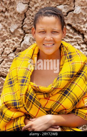 Una giovane donna di san boscimani del Kalahari centrale, villaggio di New Xade in Botswana, avvolta su una coperta gialla nel cortile della casa dopo il trasferimento Foto Stock