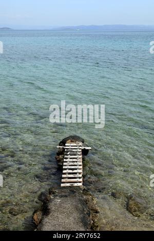 Piccolo pontile di legno ricchissimo su una costa rocciosa, vicino a Megalochori, Agistri, gruppo delle Isole Saroniche, Grecia. Presa nel luglio 2023 Foto Stock