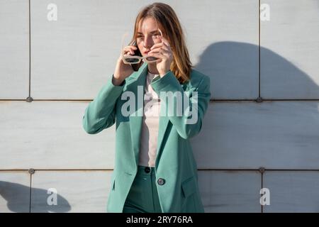 Giovane donna dai capelli allo zenzero con tuta verde che parla su smartphone in piedi su sfondo marmo Foto Stock