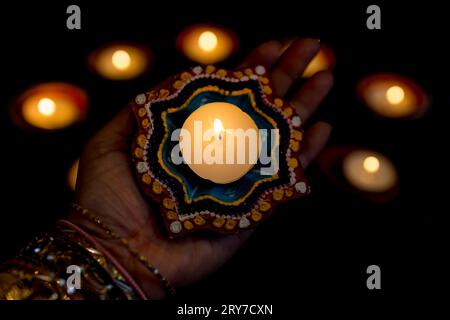 Happy Diwali - donna mani con henné che tiene accesa candela isolata su sfondo scuro. Le lampade Clay Diya si sono accese durante Deepavali, il festival indù delle luci. Foto Stock