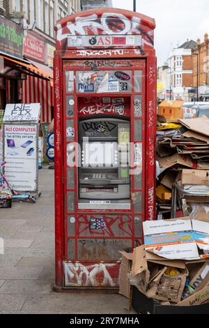 Iconica cabina telefonica rossa trasformata in un distributore contante circondato da scatole di cartone scartate a Deptford High Street, Londra Foto Stock