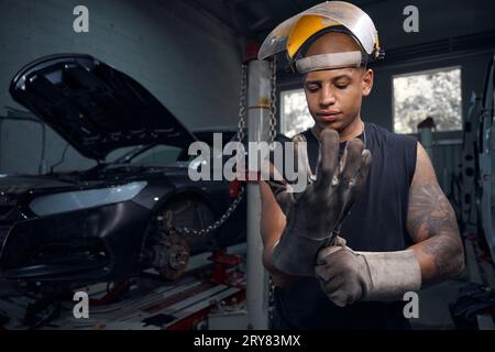 Riparatore afroamericano che salda posti arrugginiti sulla macchina Foto Stock