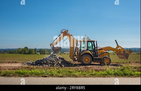 Escavatore con pala gommata con sfondo durante i lavori di movimento terra, costruzione. La terna universale ha sollevato la benna sui contro Foto Stock