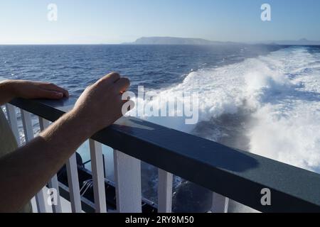 Ringhiere della nave con due mani appoggiate su di essa. Sullo sfondo c'è l'acqua di chiglia. Foto Stock