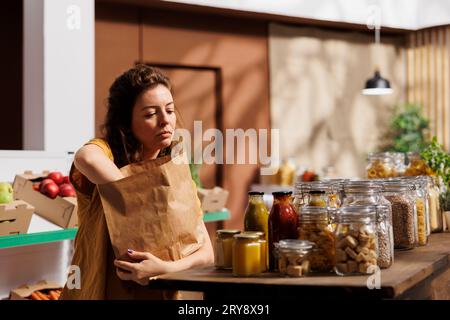 Acquirente che acquista con attenzione e preleva alimenti biologici in un negozio con rifiuti zero utilizzando sacchetti di carta per ridurre al minimo l'utilizzo di plastica. Cliente ecologico alla ricerca di verdure fresche e prive di prodotti chimici Foto Stock