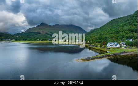 Panorama aereo del lago d'acqua dolce loch Leven con il villaggio di Glen Coe, sopra di esso, il Pap of Glencoe, Highlands, Scozia, alto 742 metri Foto Stock