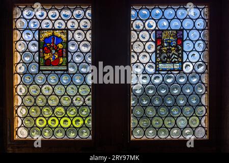 Due finestre rotonde a bulbo con stemmi araldici in vetrata illuminano quella che è probabilmente la Sala dei Bailiff (Salle des baillis) nel castello di Gruyères a Épagny vicino a Gruyères, nel cantone di Friburgo, Svizzera. Ricerche indicano che le vetrate araldiche colorate datano dal 1685, come il resto degli arredi della sala. Costruito nel XIII secolo, il castello fu la sede dei conti di Gruyère fino al 1554. Dal 1938 appartiene al cantone di Friburgo e funge da museo. Foto Stock