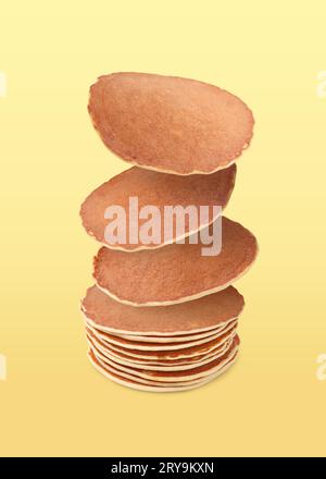 Molti gustosi pancake freschi che cadono su sfondo giallo chiaro Foto Stock