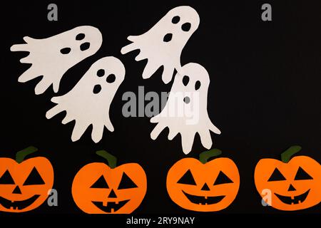 fantasmi di carta che volano sulle zucche su uno sfondo nero, concetto di halloween con artigianato e decorazioni Foto Stock