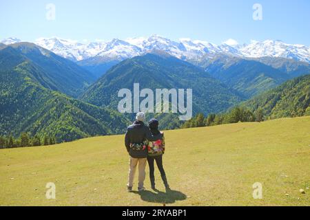 Coppia che si rilassa sul prato di Highland Farm godendo di una fantastica vista delle catene montuose del Caucaso, Mestia, regione di Svaneti, Georgia Foto Stock