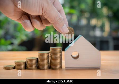Mano di un uomo d'affari che mette o risparmia denaro, monete e case modello. Investimenti immobiliari e mutui immobiliari finanziari, investimenti immobiliari, tasse A. Foto Stock
